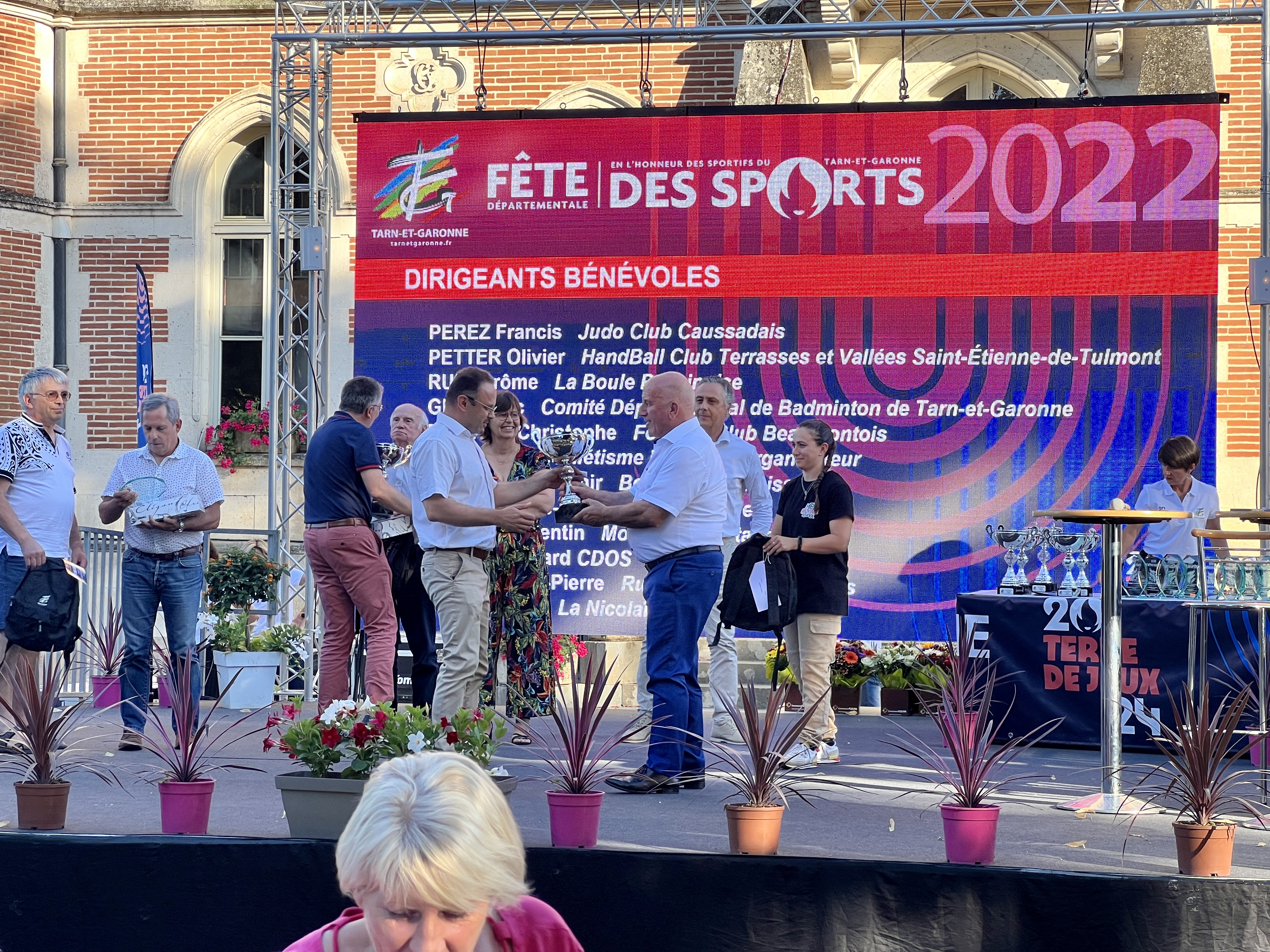 Le président sur scène qui remet une coupe aux lauréats "dirigeants bénévoles" en compagnie de nombreux élus 