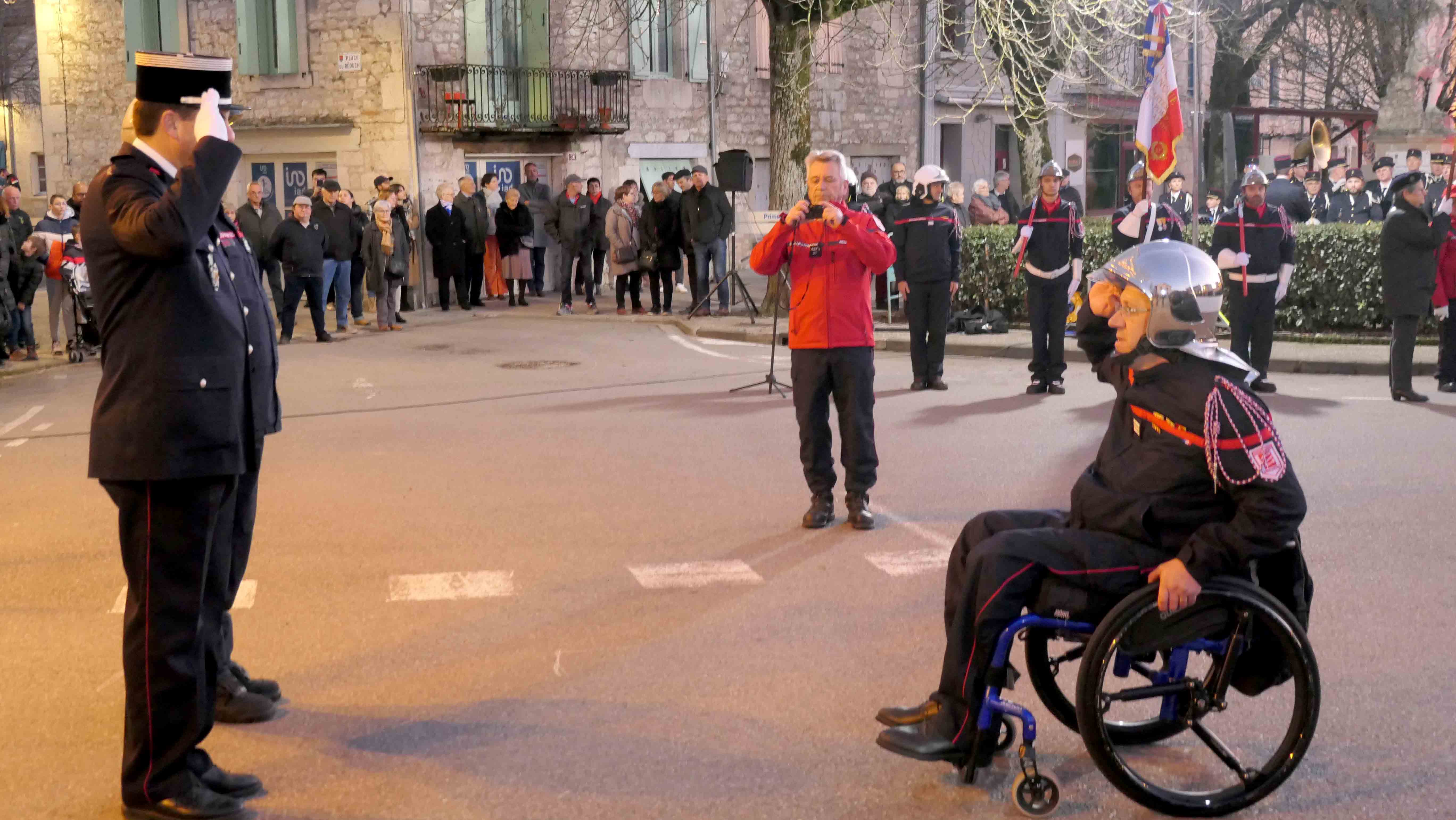 Deux pompiers debout qui saluent un pompier en fauteuil roulant 