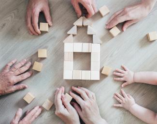 Maisons des Solidarités Un groupe de personnes de différents âges travaillant ensemble pour construire une petite maison avec des cubes en bois