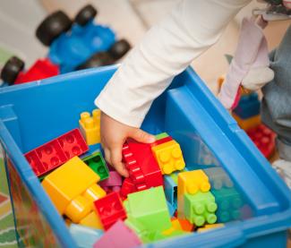Un enfant qui prend dans sa main des briques de contruction type « Lego »