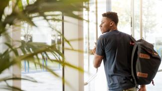 Etudiant avec un sac à dos debout devant une porte vitrée