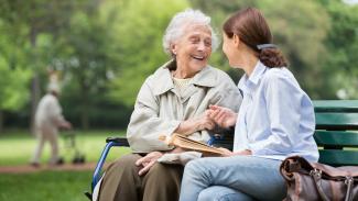 Jeune femme discutant avec une femme âgée sur un banc dans un parc, partageant un moment sincère de compagnie Jeune femme discutant avec une femme âgée sur un banc dans un parc, partageant un moment sincère de compagnie