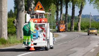 Agent de la voirie utilisant un engin pour mettre en place des plots de chantier sur la route