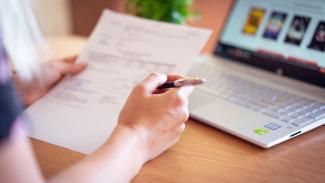 Appel à Projets Une personne assise à un bureau, tenant un feuille de papier entre ses mains, à côté d'un ordinateur portable
