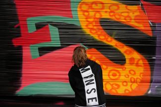 Une dame de dos en train de réaliser un graffiti sur une banderole 