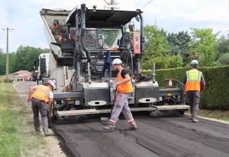 Observation d'un chantier innovant sur la route départementale 29 à Labarthe Des employés en train d'étaler du goudron sur la route avec une machine spécialisée