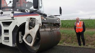 Visite d'un chantier expérimental à Génébrières Michel Weill qui regarde le bulldozer en train d'aplatir le goudron à Génébrières