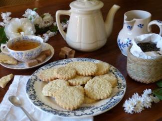 Une table avec une assiette de biscuits, une tasse de thé, une carafe et une théière