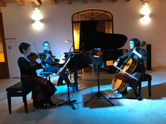 Concert par "Le Trio Lesage" à l'espace des Augustins Une violoniste assise, un pianiste assis devant son piano et une violoncelliste assise également. Tous les trois sont en train de jouer