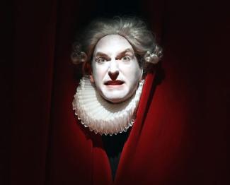 Pièce de Théâtre "Le Montespan" à l'espace des Augustins le 24 avril 2024 Un homme avec la tête qui sort de rideaux rouges portant une collerette et maquillé de peinture blanche sur le visage avec un regard tenace