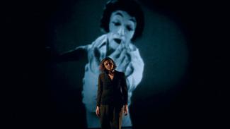 Projection du film documentaire "L'art du silence" à l'espace des Augustins Une dame avec la tête penchée qui ferme les yeux et derrière elle sur un écran un gomme maquillé en blanc et noir qui tend sa main pour "essayer" de toucher la dame