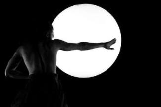 Spectacle de danse "Reflet" à l'espace des Augustins le 5 avril 2024 Un homme de dos dans le noir qui tend son bras devant une boule illuminée