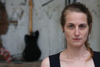 Concert par "ECCHYMOSE ROSE" Programme de l'Étonnant Été 2023 Photo du buste d'une femme de face avec une guitare à l'arrière