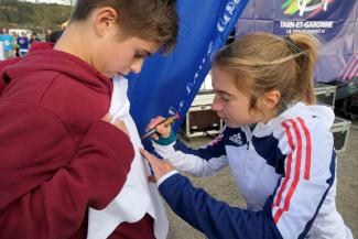 Un Cross Départemental UNSS sur la Base de Loisirs du Tarn et de la Garonne L'athlète Mathilde Sagnes en train de dédicacer le t-shirt d'un élève participant au Cross départemental UNSS organisé sur la base de loisirs du Tarn et de la Garonne le 22 novembre 2023