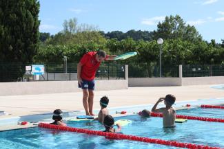 Photo d'une activité natation avec la présence d'un maître nageur Un maître-nageur hors de l'eau en train d'apprendre le crawl à des enfants dans la piscine