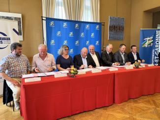 Signature du pacte d’engagement des acteurs des infrastructures de mobilité Plusieurs personnalités assis à une table rouge avec un fond comportant le logo du CD de Tarn-et-Garonne