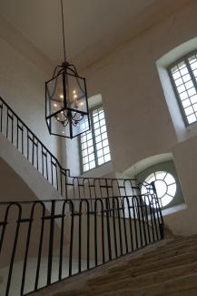 Photo d'un escalier présent à l'Abbaye de Belleperche Un escalier blanc disposant d'un rempart noir avec 3 fenêtres sur le mur