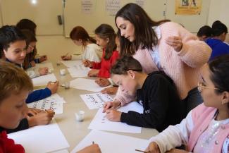 Enfants réalisant une activité de calligraphie au sein de l'Abbaye de Belleperche Plusieurs enfants entrain de réaliser une activité de calligraphie avec une animatrice
